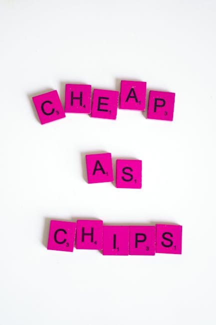 A photograph displays the word 'CHEAPAS' spelled out with small, square, bright pink tiles featuring black letters and point values typical of Scrabble game tiles, arranged on a plain white background
